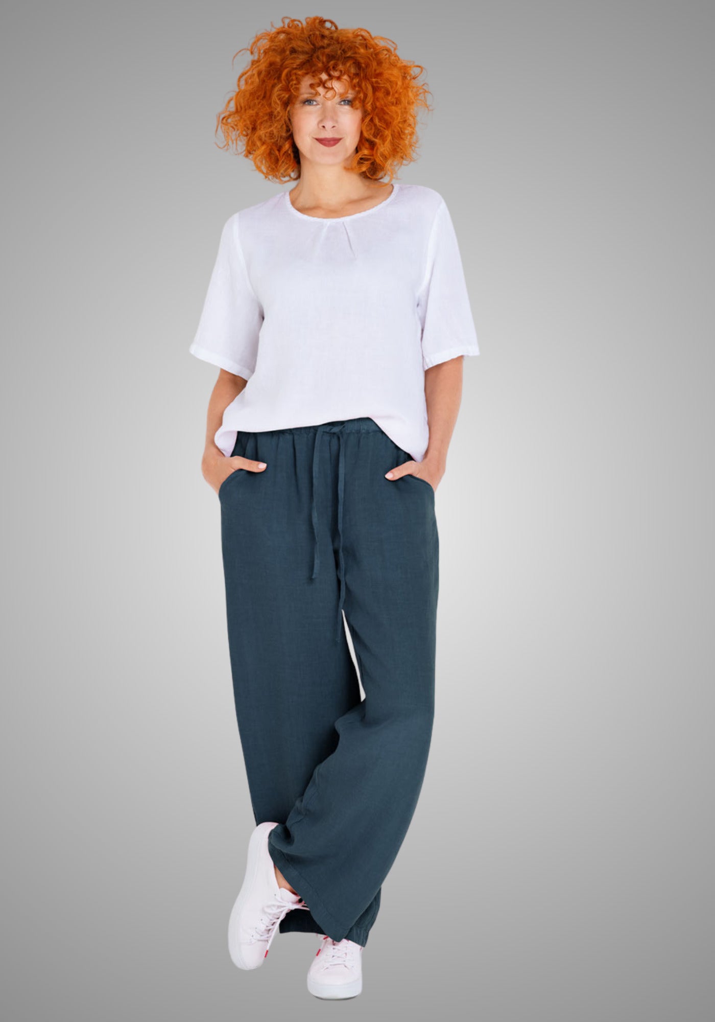 Model trägt eine locker fallende Leinenhose in dunklem Denimblau, kombiniert mit einem weißen Shirt. Die Hose hat eine Seitenlänge von ca. 106 cm in Größe M und bietet dank reinem Leinenmaterial ein luftiges Tragegefühl.