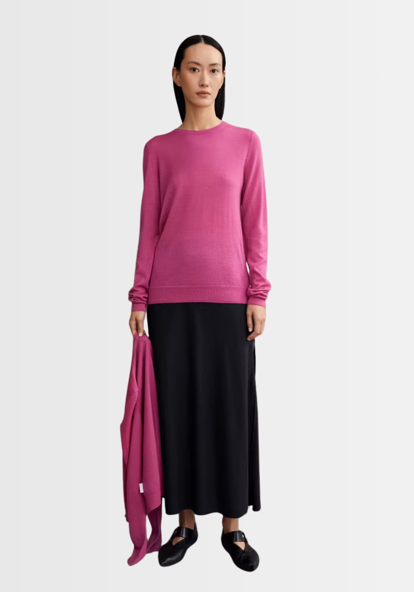 Frau präsentiert den schmal geschnittenen Merinopullover Eldiaa in kräftigem Beerenpink, kombiniert mit einem langen schwarzen Rock für einen eleganten Look.