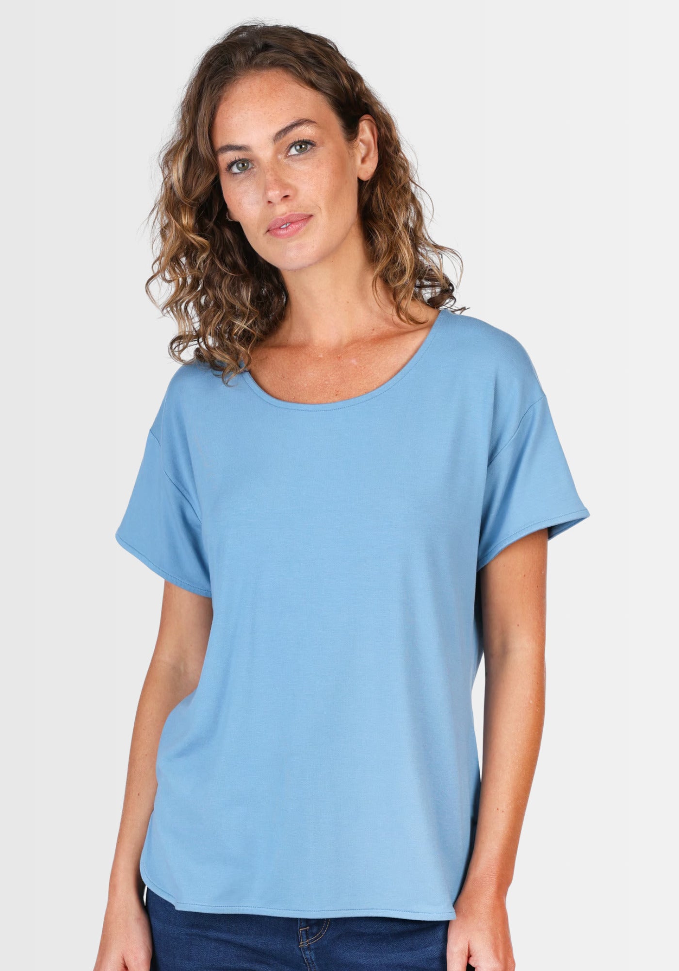 Frau lacht in die Kamera und präsentiert das T-Shirt „Betzi“ in Schwedischblau, das dank seines lässigen Kurzarmdesigns perfekt zu Jeans oder Rock passt.