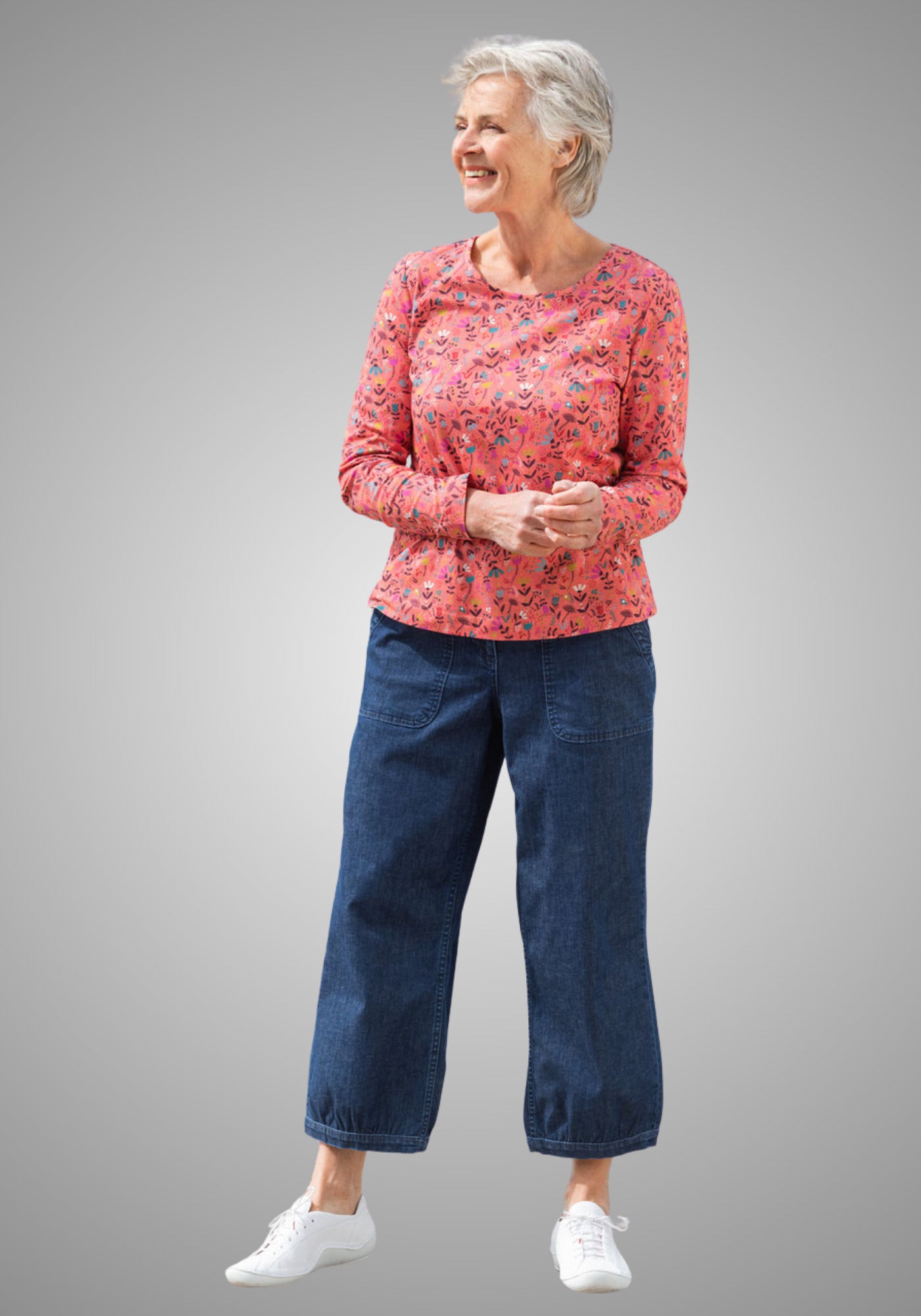 Model kombiniert die denimfarbene Pumphose aus nachhaltiger Herstellung von Heidekönigin mit einem farbenfrohen Langarmshirt für ein entspanntes Freizeitoutfit.