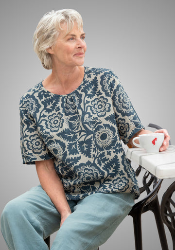 Frau trägt das dunkelblaue Blusenshirt "Tinna" aus 100% Leinen mit floralen Mustern, Rundhalsausschnitt und kurzen Ärmeln, ideal für entspannte Tage.