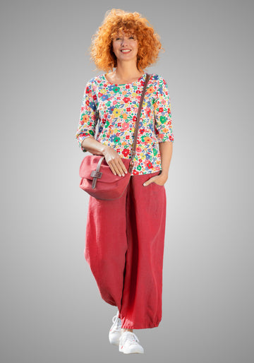 Model kombiniert die granatrote Leinenhose mit einem bunten Shirt und weißen Sneakern, für einen frischen, bequemen Sommerlook.