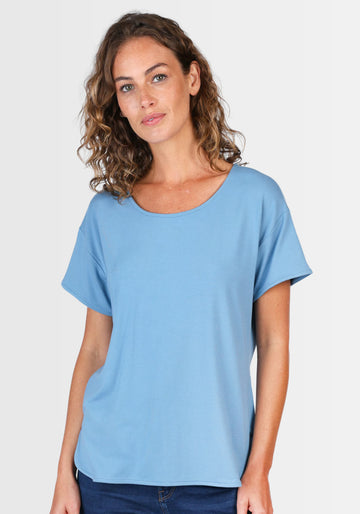 Frau lacht in die Kamera und präsentiert das T-Shirt „Betzi“ in Schwedischblau, das dank seines lässigen Kurzarmdesigns perfekt zu Jeans oder Rock passt.