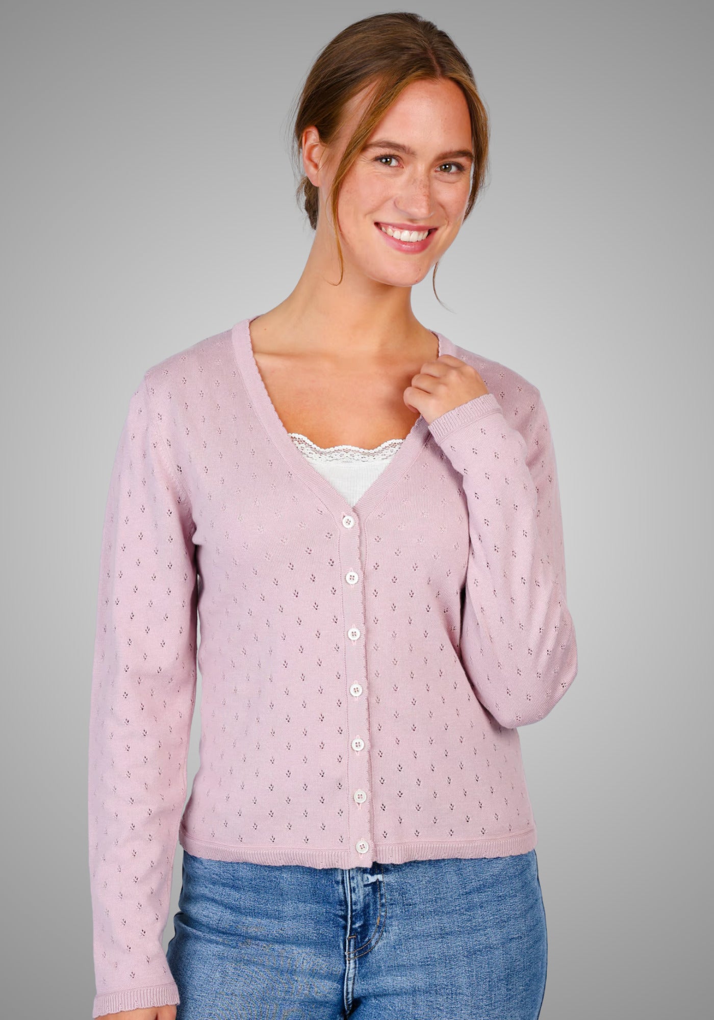 Frau trägt die Strickjacke "Amily" in zartem Rosa, gefertigt aus 50 % Baumwolle und 50 % Modal, mit kunstvollem Ajourmuster, V-Ausschnitt und Knopfleiste – perfekt für einen femininen Look.